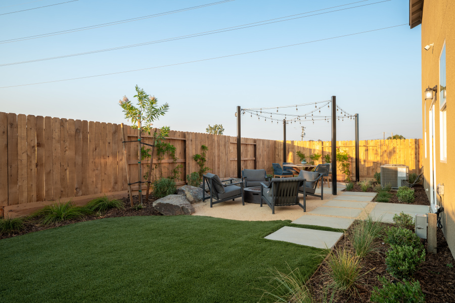 A backyard with a fence and a patio with chairs and a table.