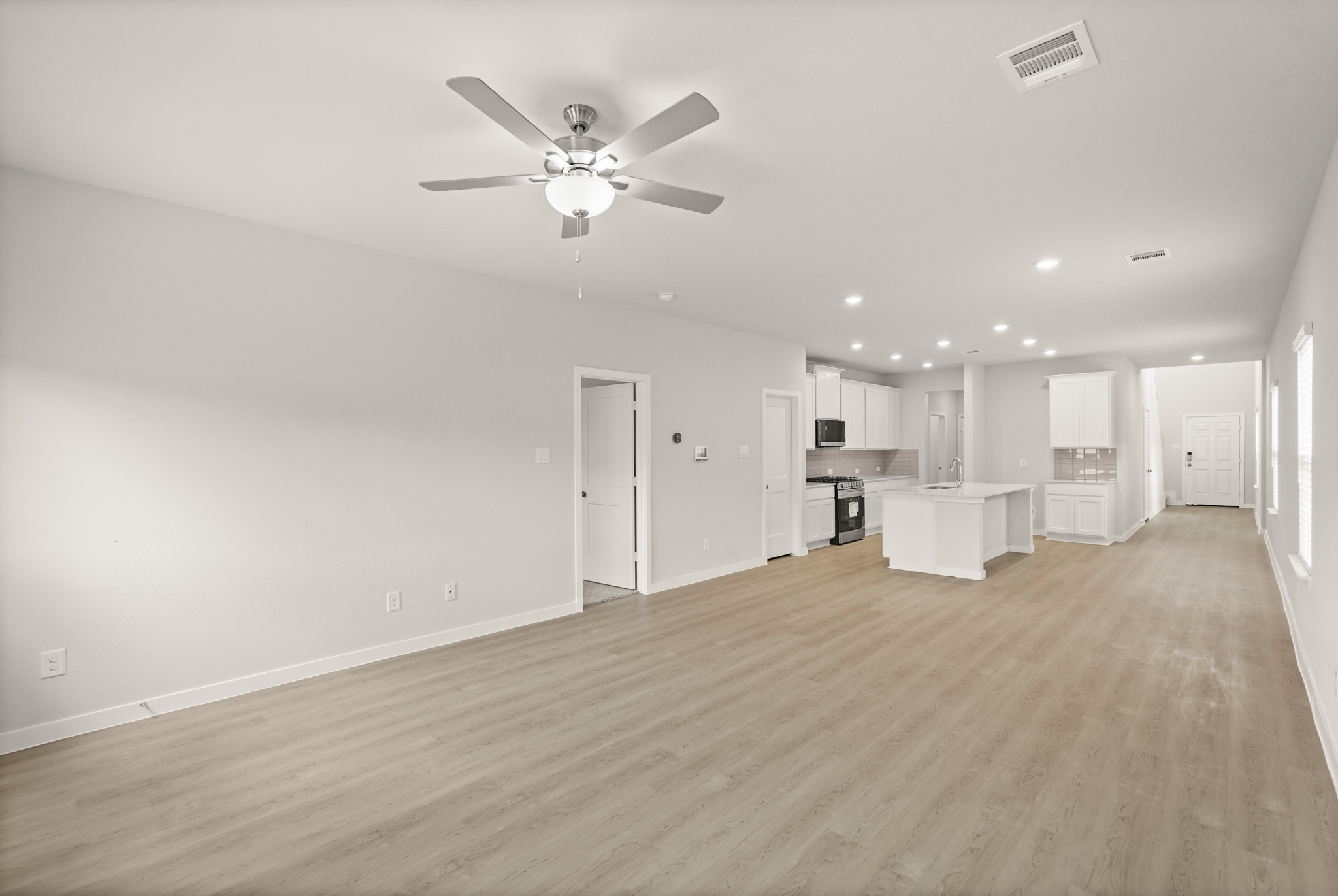 A large empty room with a ceiling fan and a wood floor.