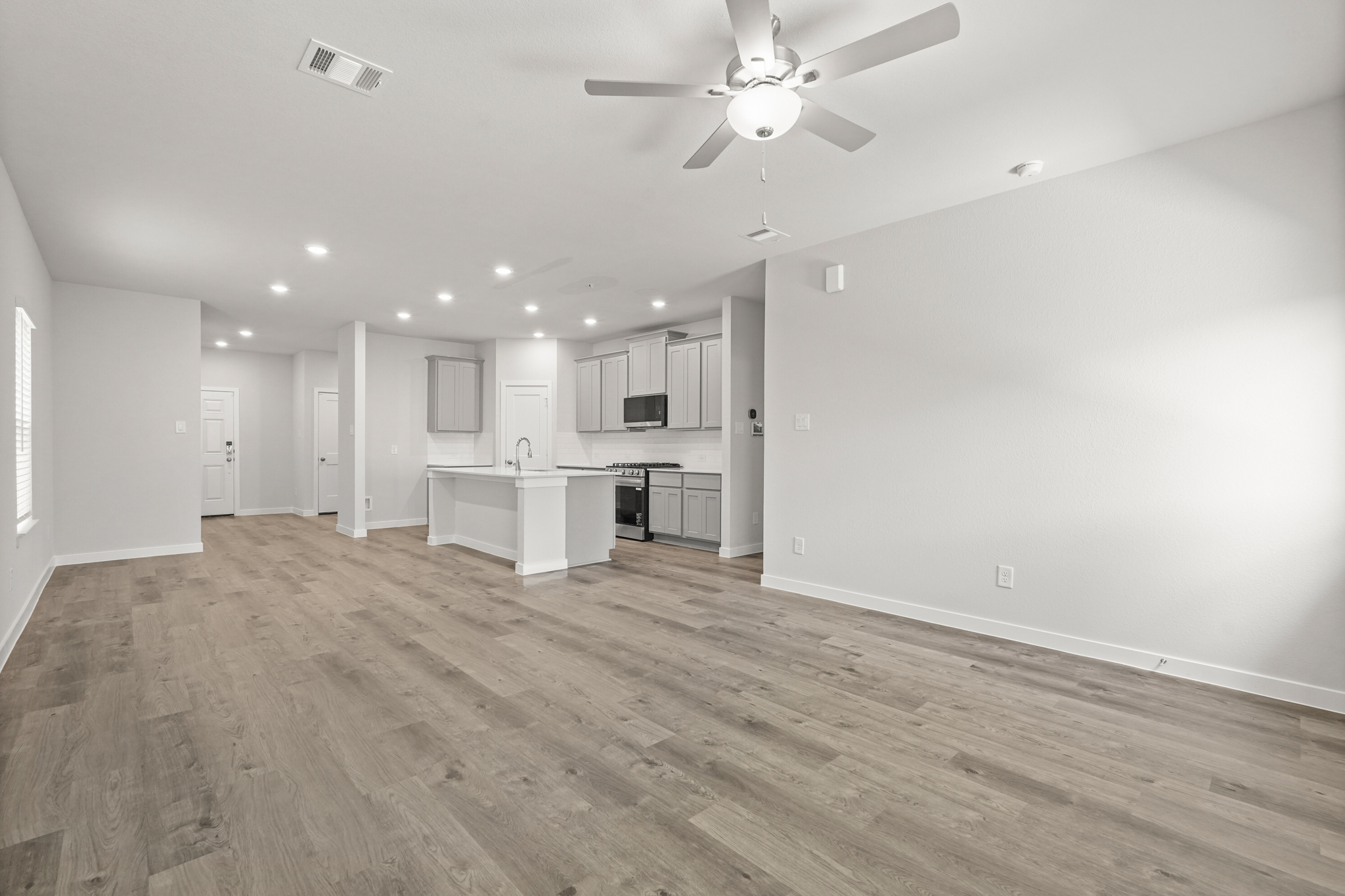 A large empty room with a ceiling fan and a wood floor.