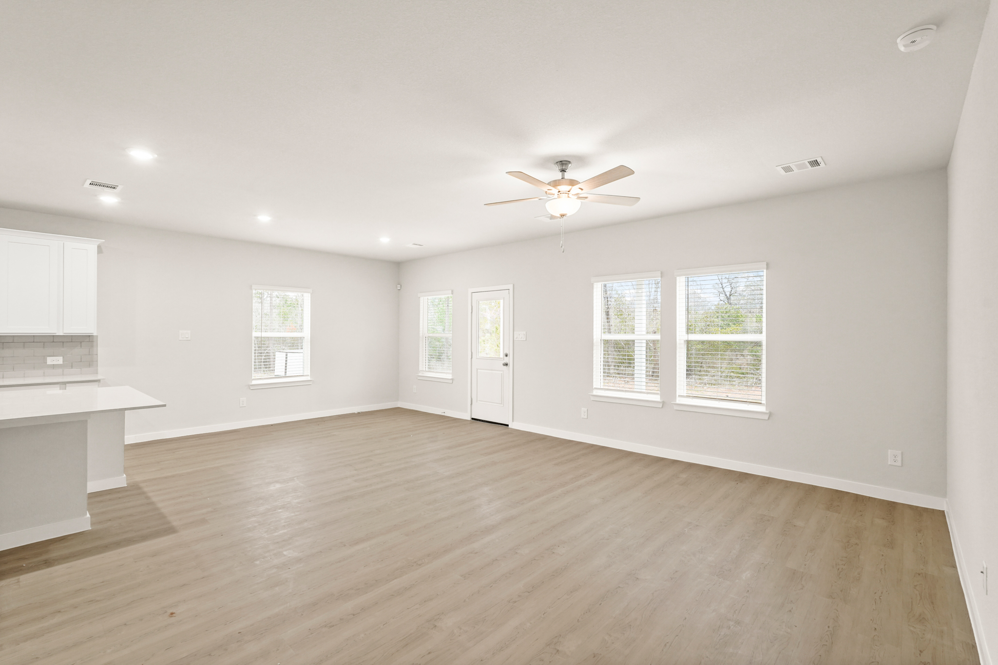 A large empty room with a wood floor and a ceiling fan.