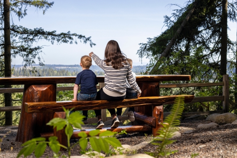A person and a boy sitting on a bench overlooking a city.